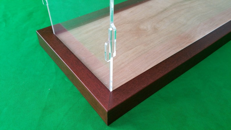 Op de afbeelding: Een transparante acryl displaykast met een houten basis. De kast heeft een donkerbruin houten frame en een transparant acryl deksel. De kast staat op een groene ondergrond.