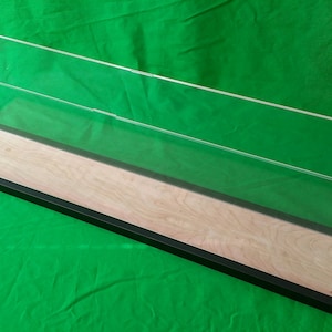 Puede incluir: Una vitrina de exhibición de acrílico transparente con una base de madera y un borde negro. La vitrina está vacía y lista para exhibir tus objetos de colección.