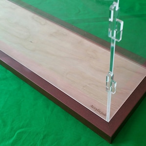May include: A clear acrylic display case with a wooden base. The base is a light brown color and has the word "AcrylicJob" engraved on it.