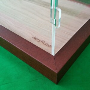 Op de afbeelding: Een houten displaykast met een transparant acrylaatdeksel en een bruine houten basis. De basis heeft de tekst "Acrylicjob" gegraveerd.