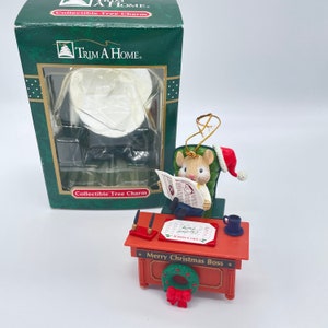 May include: A Christmas ornament featuring a mouse wearing a Santa hat sitting in a green chair and reading a newspaper. The mouse is sitting at a red desk with a calendar, a pen, and a coffee cup. The desk has a wreath and the text "Merry Christmas Boss".