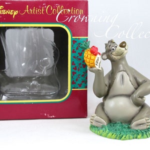 May include: A gray resin figurine of Baloo the bear from Disney's The Jungle Book. Baloo is sitting on a green base and holding a pineapple with a red bow and a tag that says "From Baloo".