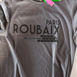 May include: Grey t-shirt with black text that reads "Paris Roubaix Hell of the North". The shirt has a green tag that says "pure organic".