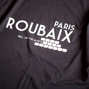 May include: Black t-shirt with white text that reads "Roubaix Paris Hell of the North" and a graphic of a cobblestone road.