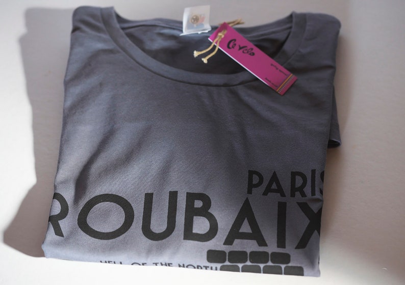 May include: A grey t-shirt with black text that reads "Roubaix" and "Paris" with the words "Hell of the North" underneath.