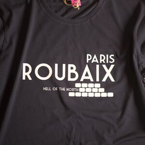 May include: A dark grey t-shirt with white text that reads "Paris Roubaix Hell of the North" with a graphic of a brick wall.