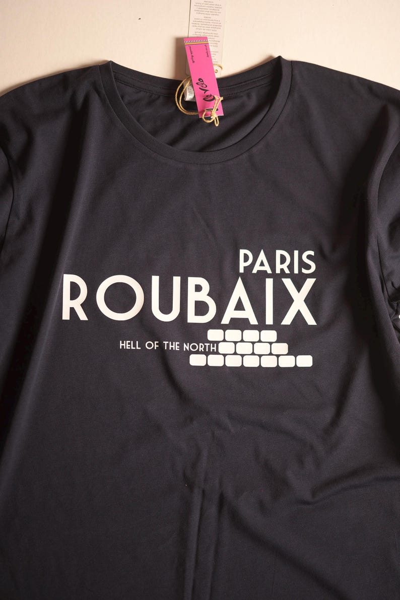 May include: A dark grey t-shirt with white text that reads "Paris Roubaix Hell of the North" with a graphic of a brick wall.