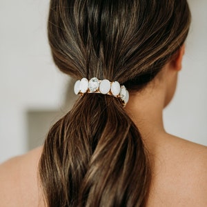 May include: A brown ponytail holder with a row of clear and white oval-shaped rhinestones.