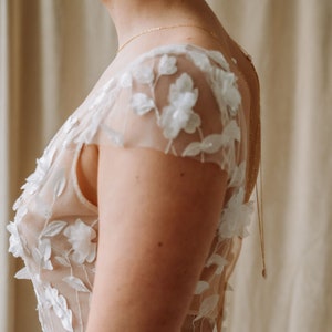 May include: A white wedding dress with a sheer bodice and floral embroidery. The dress has a fitted silhouette and a low back.