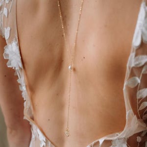 Op de afbeelding: Een delicate gouden rugketting met een kleine parel en een bloemmotief aan de onderkant.