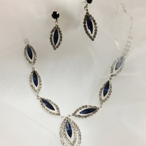 May include: A silver necklace and earrings set with dark blue marquise-shaped stones surrounded by clear rhinestones.
