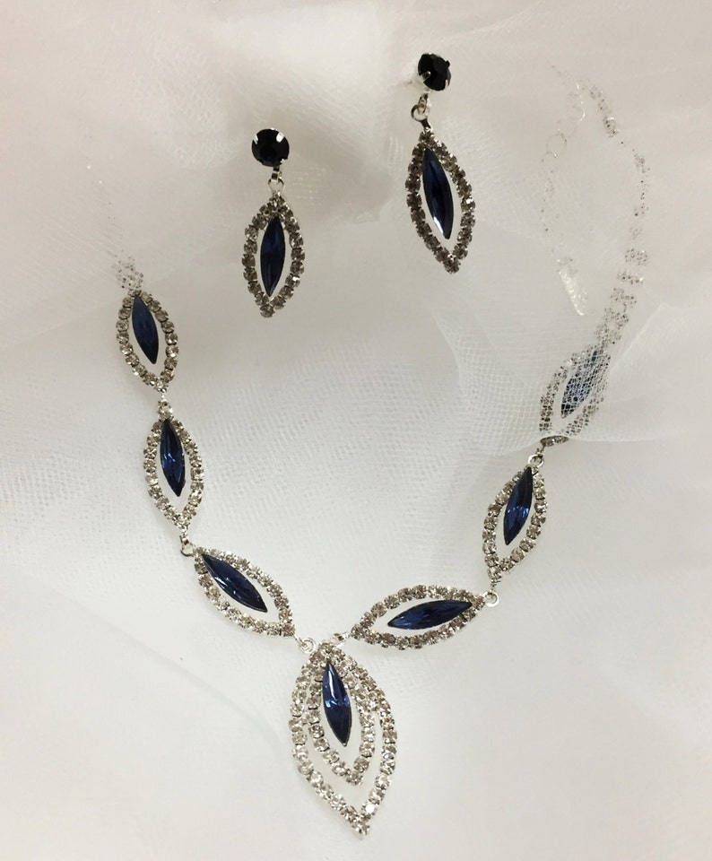 May include: A silver necklace and earrings set with dark blue marquise-shaped stones surrounded by clear rhinestones.