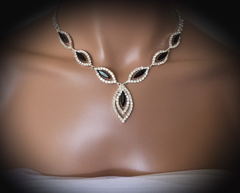 May include: A silver necklace with a black crystal pendant. The necklace is made of small clear crystals and has a teardrop shape.
