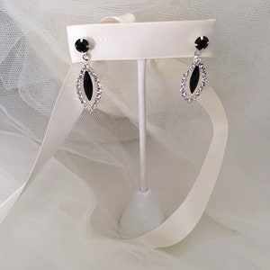 May include: A pair of silver earrings with black oval-shaped stones surrounded by clear rhinestones.