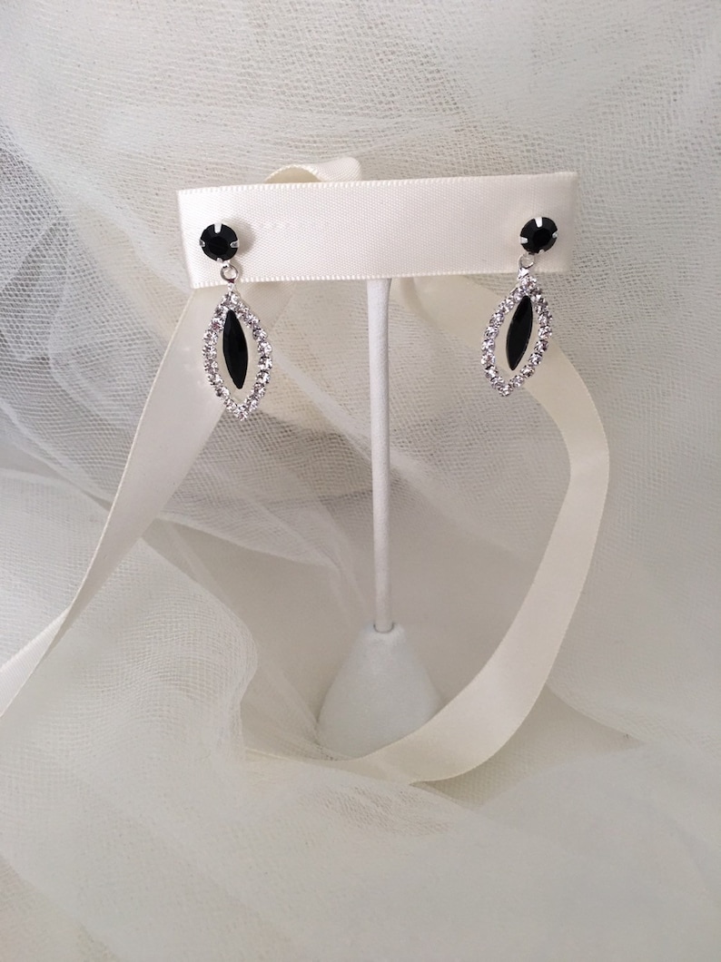 May include: A pair of silver earrings with black oval-shaped stones surrounded by clear rhinestones.