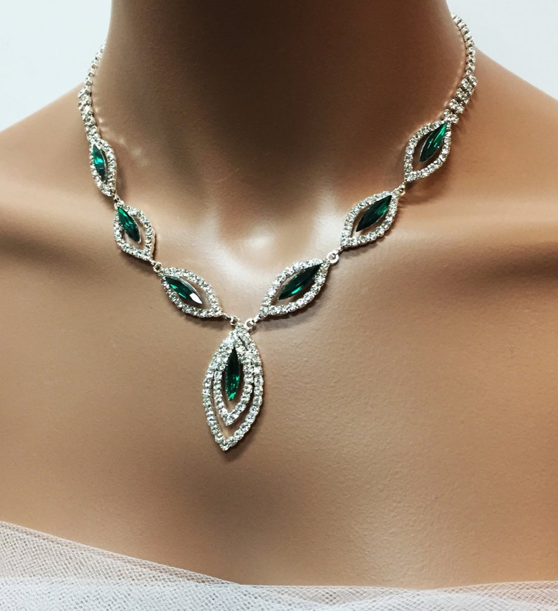 May include: A silver necklace with a teardrop pendant featuring multiple emerald green stones surrounded by clear rhinestones.