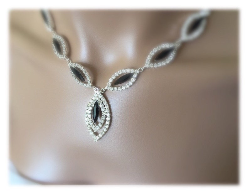 May include: A silver necklace with a black crystal pendant. The necklace is made of small, clear crystals and has a delicate design.