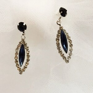 May include: A pair of silver dangle earrings with a dark blue marquise-shaped stone set in a clear rhinestone halo.