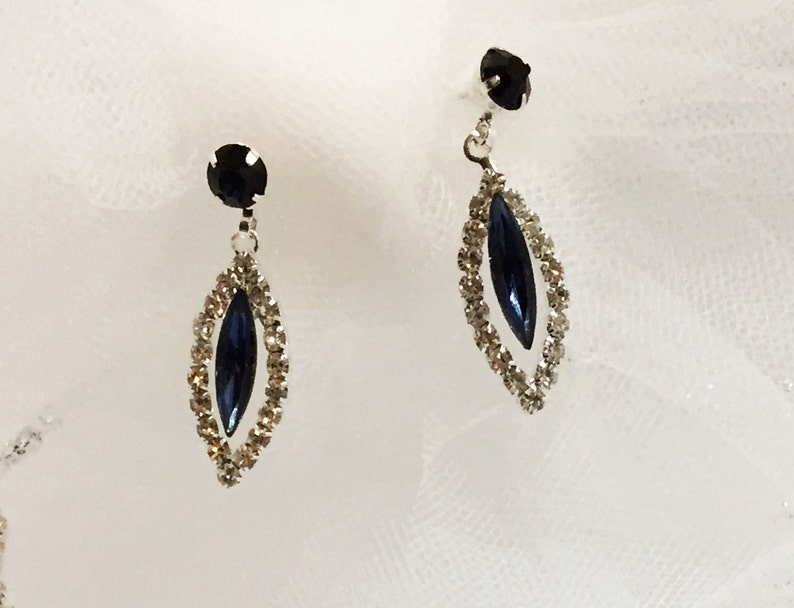 May include: A pair of silver dangle earrings with a dark blue marquise-shaped stone set in a clear rhinestone halo.