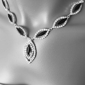 May include: A silver necklace with a black stone pendant. The necklace is made of small, clear rhinestones and has a teardrop-shaped pendant.
