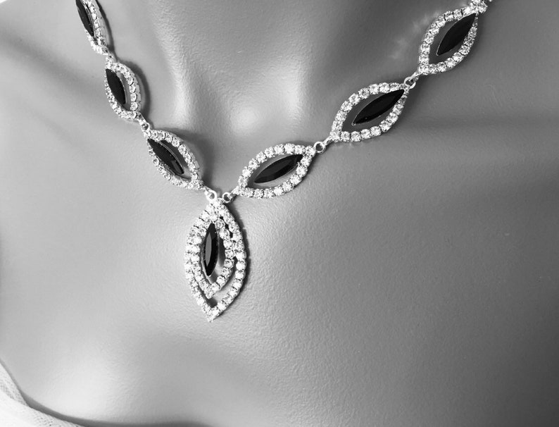 May include: A silver necklace with a black stone pendant. The necklace is made of small, clear rhinestones and has a teardrop-shaped pendant.
