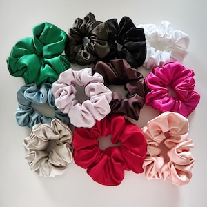 May include: Assortment of 11 colorful satin scrunchies in various colors, including green, blue, pink, red, brown, and black. The scrunchies are arranged in a circle on a white background.