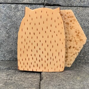 May include: A ceramic dish sponge holder shaped like an owl with a brown and tan speckled pattern. The holder has a small sponge attached to the side.