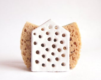 May include: White ceramic sponge holder with a geometric pattern of holes. The holder is sitting on two brown sponges.