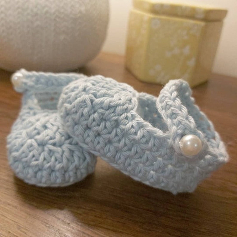 May include: A pair of light blue crocheted baby shoes with white pearl embellishments.