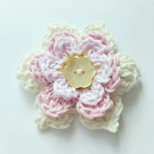 May include: A crocheted flower with pink and white yarn, featuring a pearl button in the center.