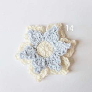 May include: A crocheted flower with a light blue center and a white outer layer. The flower has six petals and is numbered "14".