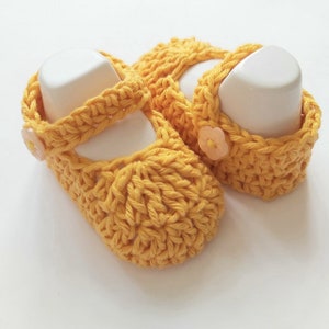 May include: A pair of yellow crocheted baby shoes with a flower button on each shoe.