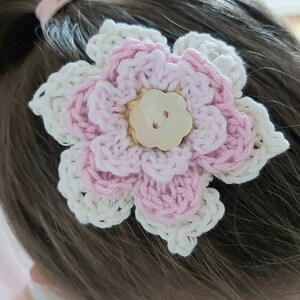 May include: A crocheted flower hair clip in pink and white with a pearl button in the center.