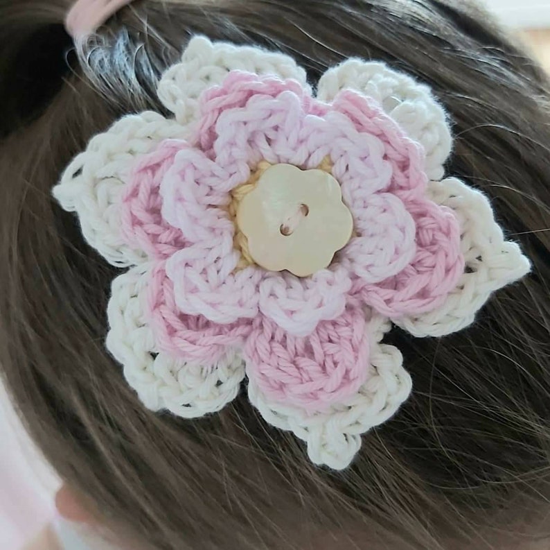 May include: A crocheted flower hair clip in pink and white with a pearl button in the center.