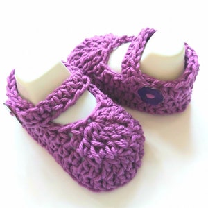 May include: A pair of purple crocheted baby shoes with a flower button on each shoe.