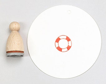 Può includere: Timbro in legno con un design di salvagente rosso e bianco. Il timbro è su uno sfondo bianco.