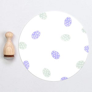 Peut inclure: Un autocollant rond blanc avec un motif répété d'œufs violets et verts à pois blancs.