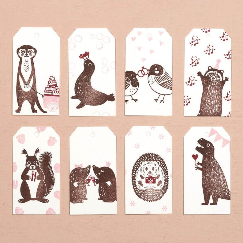 May include: Set of eight white gift tags with brown animal illustrations. The tags feature a meerkat, seal, birds, raccoon, squirrel, moles, hedgehog, and dinosaur. Each tag has a unique design with pink accents, perfect for gifts.