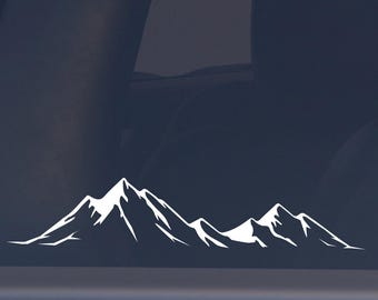 May include: White mountain range decal on a car window. The decal features a stylized outline of several mountain peaks, suggesting an outdoor or adventure theme. The design is simple and clean, suitable for vehicles.