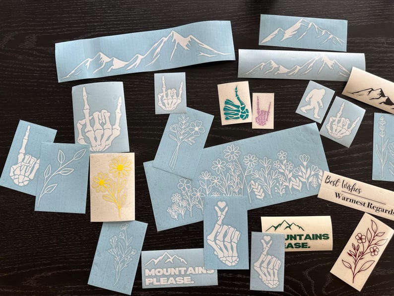 Peut inclure: Divers autocollants en vinyle bleu clair et cr&egrave;me avec divers motifs. Les autocollants pr&eacute;sentent des cha&icirc;nes de montagnes, des motifs floraux, des mains de squelette et le texte &laquo;MOUNTAINS PLEASE&raquo;. Certains autocollants ont le texte &laquo;Best Wishes, Warmest Regards&raquo;.