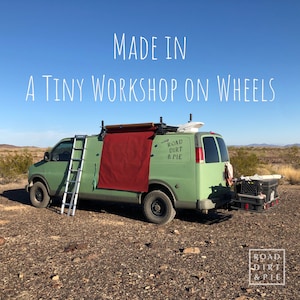A green van with red waxed canvas draped down the side. The van has a ladder on the side and a sticker on the back that says 'Road Dirt & Pie'. The van is parked in the desert with a blue sky in the background. The text 'MADE IN A TINY WORKSHOP ON WHEELS' is superimposed on the image.