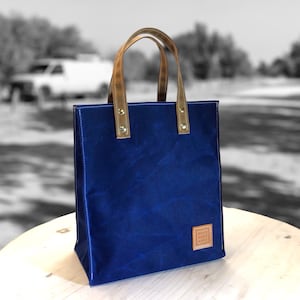 Cabas en toile cirée bleu pour homme et femme. Transportez votre déjeuner, votre petit projet et vos livres dans ce sac résistant aux intempéries. Se plie à plat. Fabriqué aux États-Unis