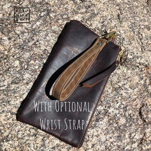 A brown leather clutch with a zipper closure and a brown wrist strap with a brass clasp. The text 'WITH OPTIONAL WRIST STRAP' is printed on the clutch.
