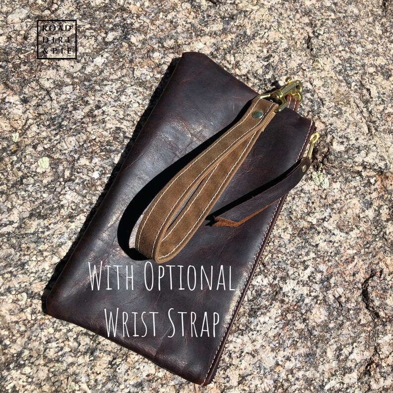 A brown leather clutch with a zipper closure and a brown wrist strap with a brass clasp. The text 'WITH OPTIONAL WRIST STRAP' is printed on the clutch.
