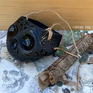 May include: Black ceramic skull planter with intricate details, hanging from a twine rope, next to a brown branch with a metal hook.  @RECHO_POR_SEGO