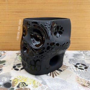 May include: Black ceramic skull planter with intricate floral designs. The planter is made of glazed ceramic and has a smooth, matte finish.