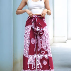 Op de afbeelding: Een vrouw draagt een wit tanktop en een bordeauxrode broek met een witte olifant en mandala print. De broek heeft een strik in de taille.