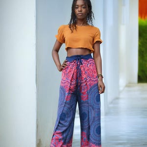 May include: A woman wearing a mustard yellow crop top and blue and pink patterned pants with a mandala design. The pants have a tie at the waist.