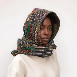 May include: A person wearing a hooded scarf with a colourful geometric pattern. The scarf is made of a soft, woven fabric and has a green lining.