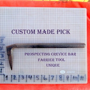 May include: A custom-made prospecting crevice bar, a farrier tool, with a unique design. The metal bar is dark with a bent, pointed end. Text on the background reads "Custom Made Pick" and "Prospecting Crevice Bar".